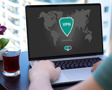 A person types on a laptop computer next to a glass of tea. The laptop screen shows a shield icon that says &quot;VPN.&quot; The screen also shows a switch that shows the VPN is turned on.